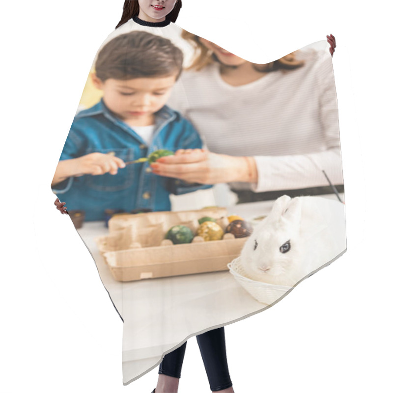 Personality  Selective Focus Of Mother And Son Painting Easter Eggs While Sitting At Table Near Bunny In Wicker Hair Cutting Cape