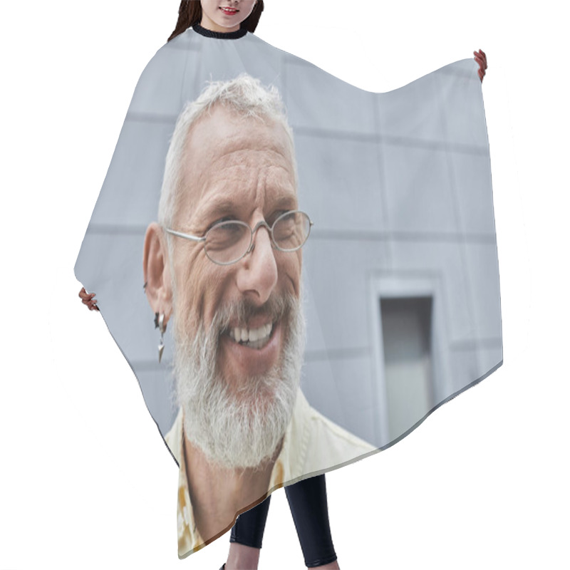 Personality  A Mature Gay Man With A White Beard, Wearing Glasses, Smiles While Standing In Front Of A Modern Building. Hair Cutting Cape