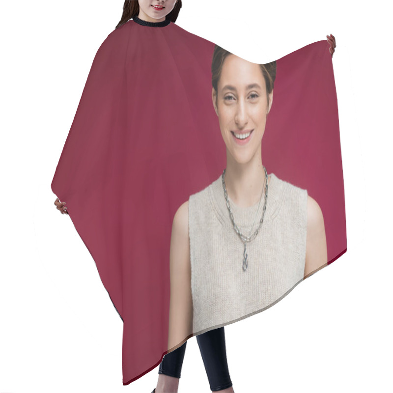 Personality  Pleased Young Woman In Sleeveless Shirt And Chain Necklace Standing On Maroon Background  Hair Cutting Cape