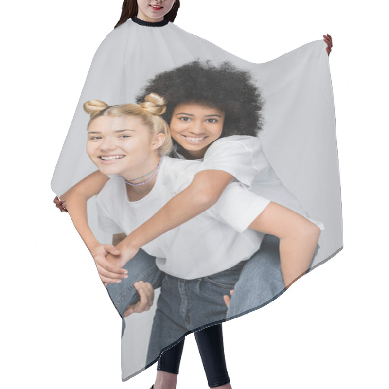 Personality  Teen African American Girl In Jeans And White T-shirt Hugging Blonde Girlfriend While Looking At Camera And Standing Isolated On Grey, Energetic Teenage Models Spending Time Hair Cutting Cape