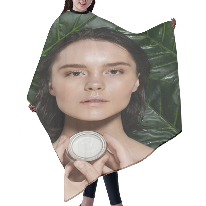 Personality  A Woman Holds A Jar Of Cream Against A Backdrop Of Vibrant Green Foliage. Hair Cutting Cape