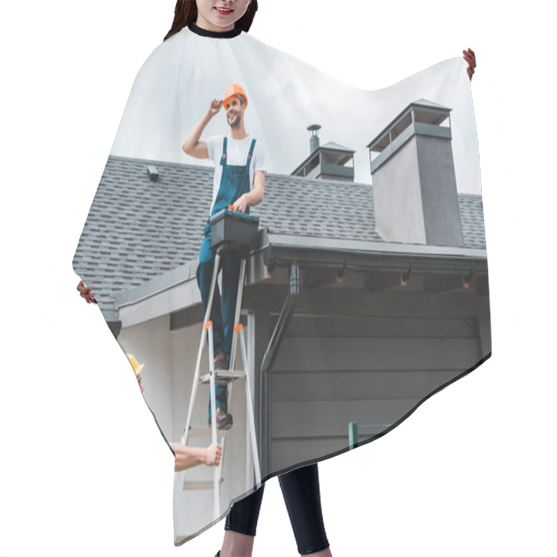 Personality  Happy Repairman Sitting On Roof And Holding Toolbox Near Coworker In Helmet Hair Cutting Cape