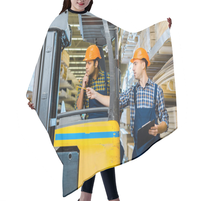 Personality  Indian Warehouse Worker Sitting In Forklift Machine Near Colleague Pointing With Pencil Hair Cutting Cape