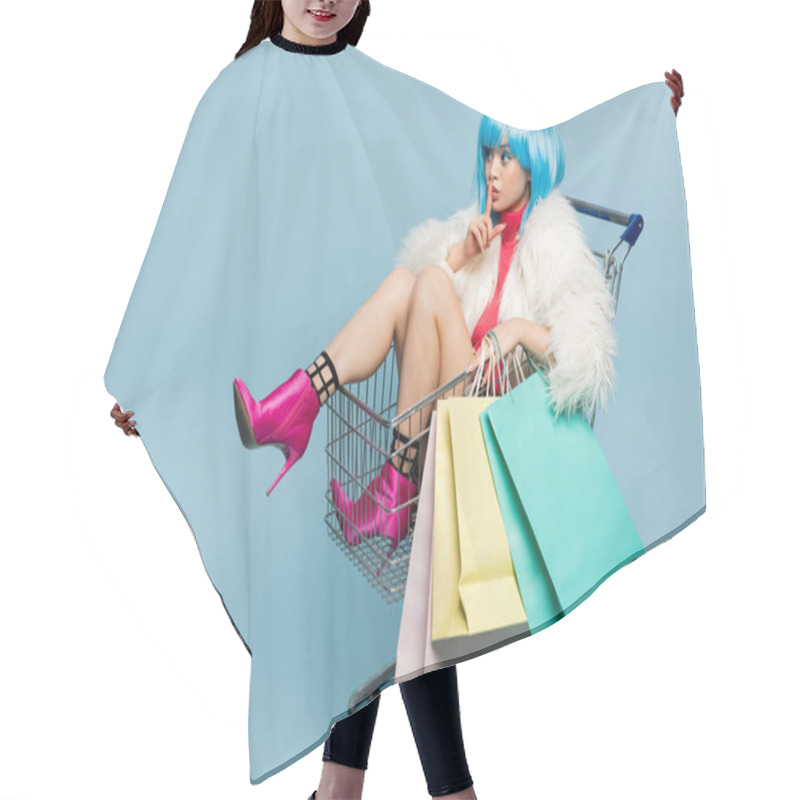 Personality  Asian Woman In Bright Wig And Furry Jacket Holding Shopping Bags In Cart And Showing Secret Gesture On Blue Background  Hair Cutting Cape