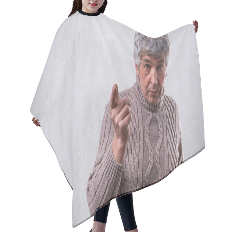 Personality  An Astonished Handsome Elderly Man With Gray Hair Dressed In Sweater Standing Near White Wall Pointing With Finger Wanting To Say Something Important. Senior Man Threatens With Finger. Displeased Man Hair Cutting Cape