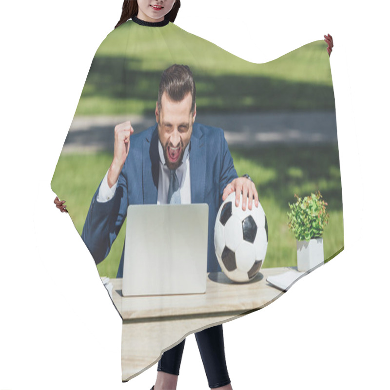 Personality  Young Businessman Sitting At Table With Laptop, Flowerpot And Glasses, Watching Football, Cheering On Team And Holding Soccer Ball Hair Cutting Cape