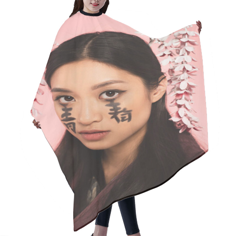 Personality  Young Asian Woman With Hieroglyphs On Face Looking At Camera Isolated On Pink  Hair Cutting Cape