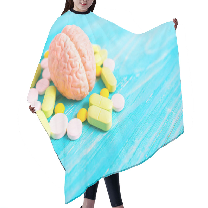 Personality  Detailed Model Of A Human Brain Surrounded By Oval And Round Pills Colored White, Green And Yellow, Placed On A Blue Wooden Background With Copy Space. Trapped Consciousness Concept. Hair Cutting Cape