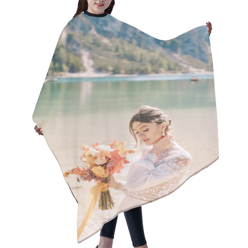 Personality  Beautiful Bride In A White Dress With Sleeves And Lace, With A Yellow Autumn Bouquet Of Dried Flowers And Peony Roses, On The Lago Di Braies In Italy. Destination Wedding In Europe, On Braies Lake. Hair Cutting Cape