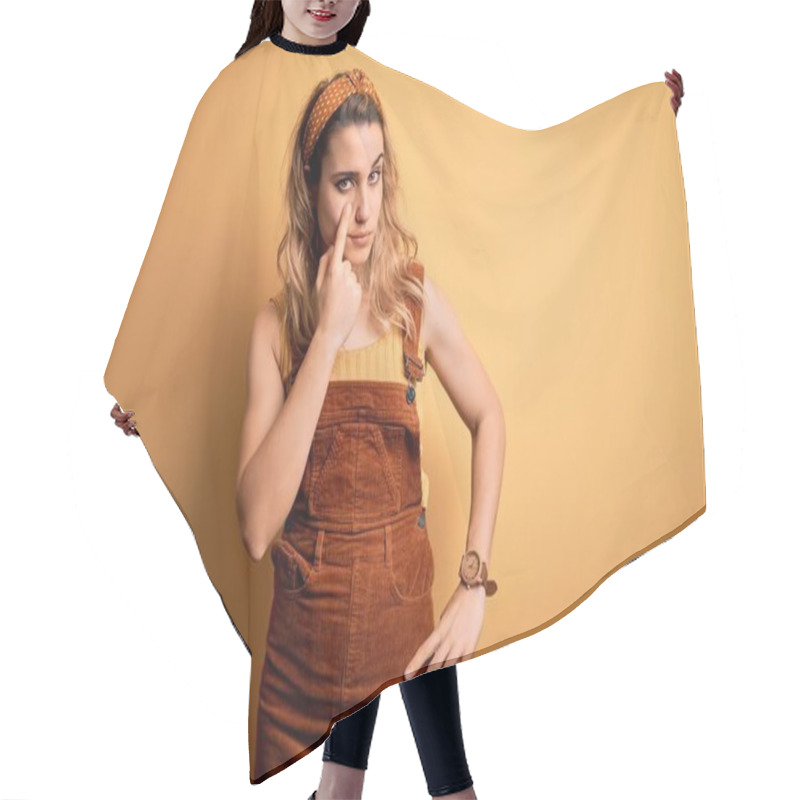 Personality  Young Beautiful Blonde Woman Wearing Overalls And Diadem Standing Over Yellow Background Pointing To The Eye Watching You Gesture, Suspicious Expression Hair Cutting Cape