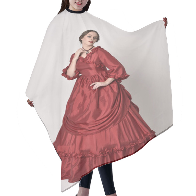 Personality  Full Length Portrait Of A Brunette Girl Wearing A Red Silk Victorian Gown. Standing Pose On A White Studio Background. Hair Cutting Cape