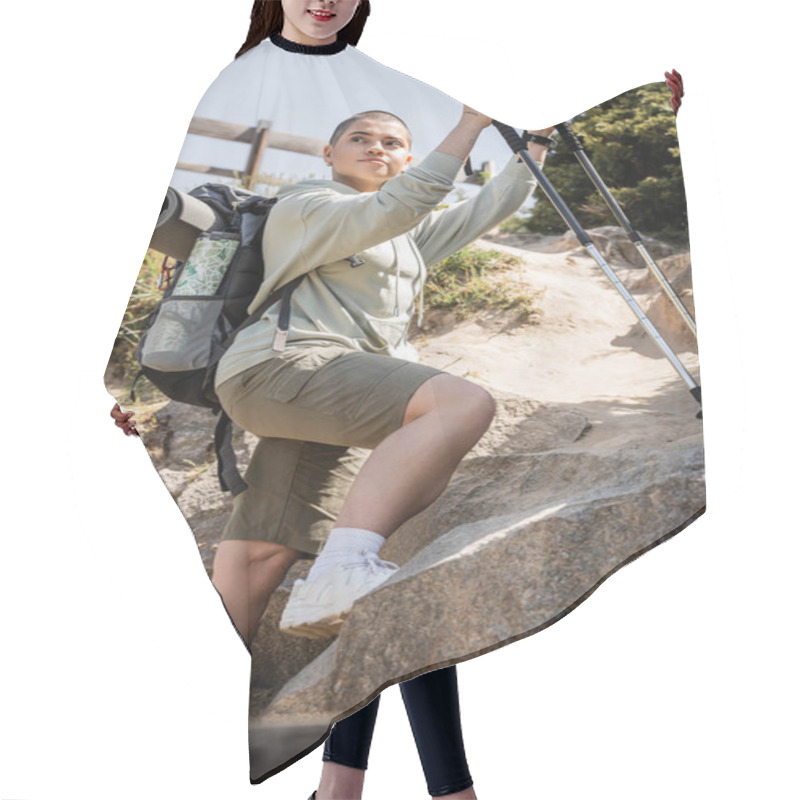 Personality  Low Angle View Of Young Short Haired Woman Traveler With Backpack Holding Trekking Poles And Looking Away While Standing Near Hill With Stones, Translation Of Tattoo: Love Hair Cutting Cape