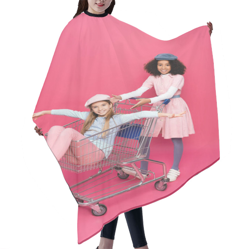 Personality  Trendy African American Girl Pointing At Happy Friend Having Fun In Shopping Cart On Pink Hair Cutting Cape