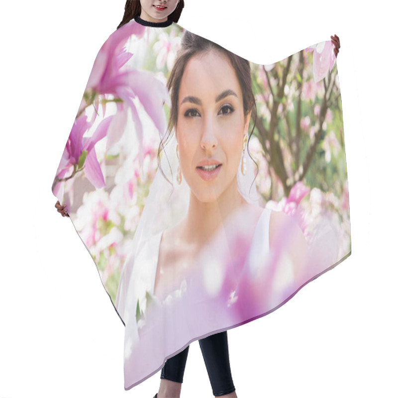 Personality  Brunette Bride Looking At Camera Near Blurred Magnolia Flowers  Hair Cutting Cape