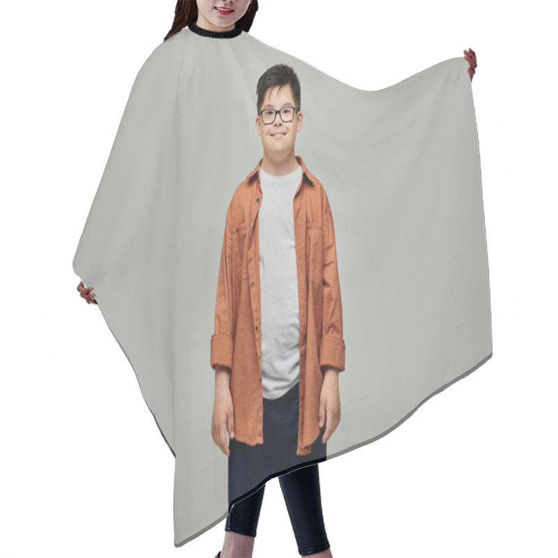 Personality  A Charming Little Boy With Down Syndrome Wearing Glasses Stands Against A Gray Background. Hair Cutting Cape