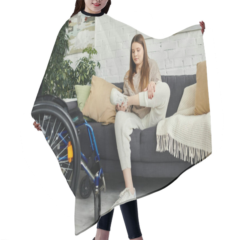 Personality  A Young Woman In A Wheelchair Puts On Her Sneakers While Sitting On A Couch In Her Living Room. Hair Cutting Cape