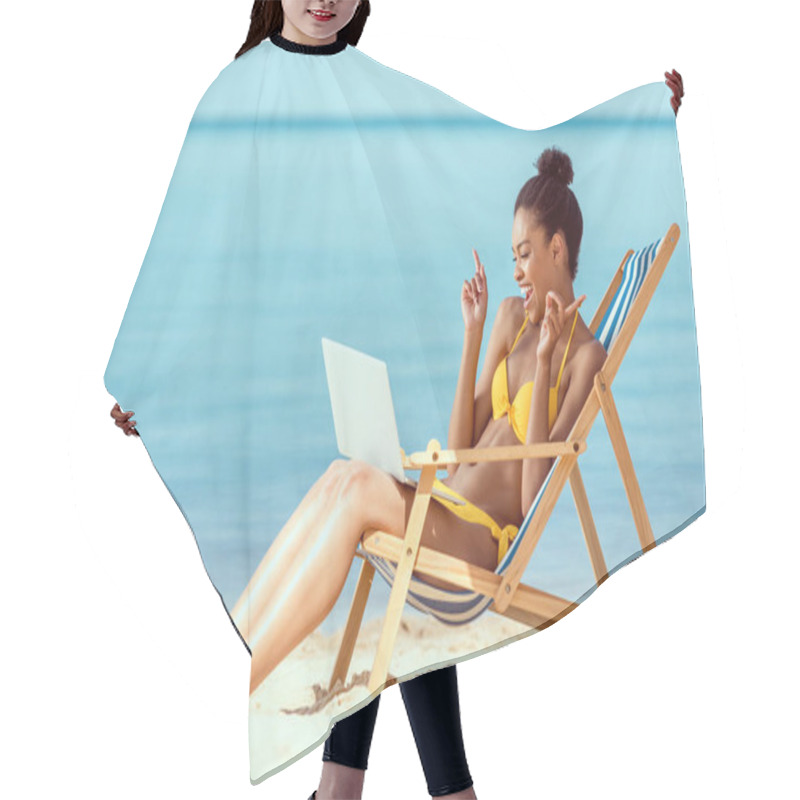 Personality  Smiling African American Woman Gesturing By Fingers And Communicating By Laptop While Sitting On Deck Chair On Sandy Beach  Hair Cutting Cape