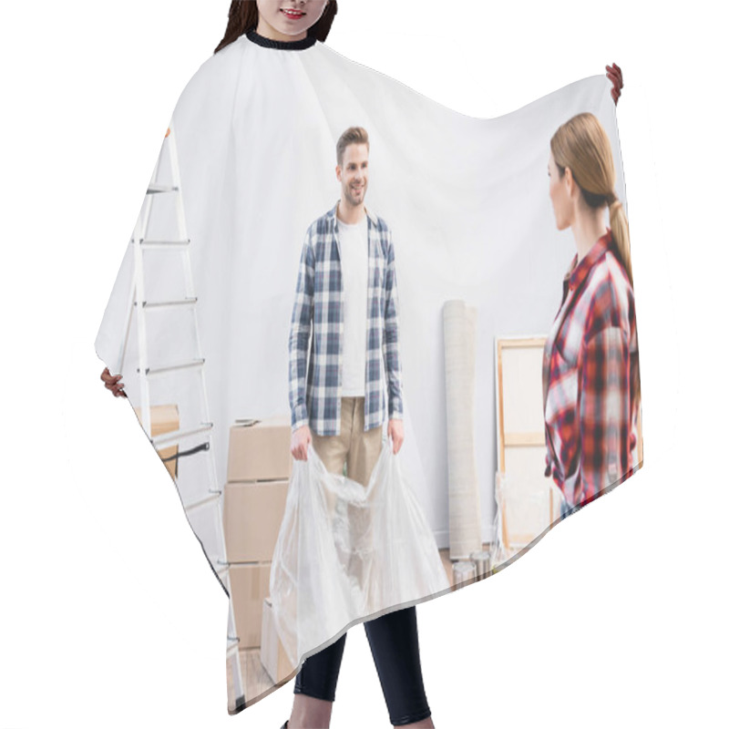 Personality  Smiling Young Man Looking At Woman While Covering Room With Polyethylene During Repair At Home Hair Cutting Cape