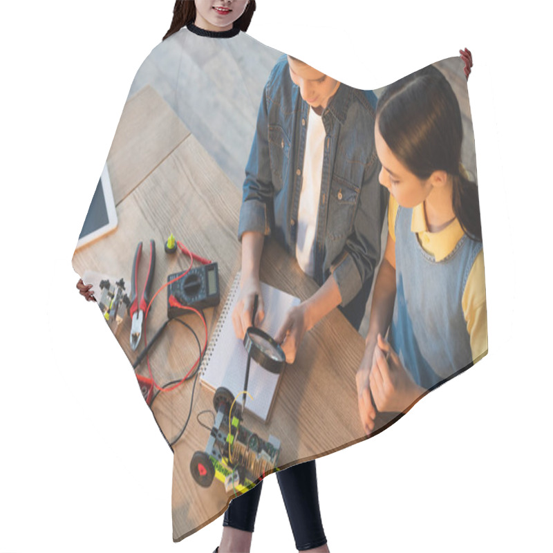 Personality  High Angle View Of Boy Holding Magnifier Near Notebook And Pointing With Pencil At Robotics Model Hair Cutting Cape