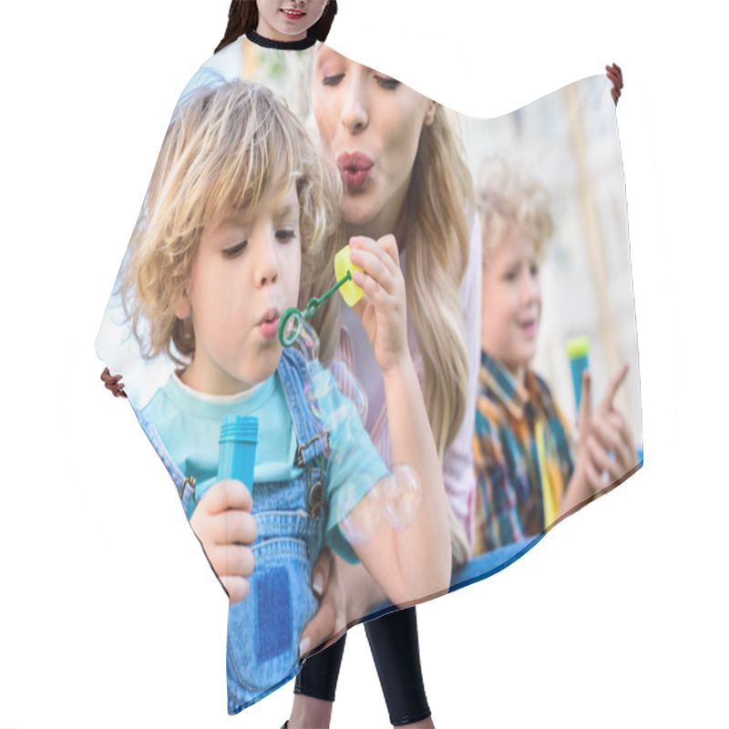 Personality  Selective Focus Of Mother And Little Son Using Bubble Blower While Other Boy Sitting Near  Hair Cutting Cape