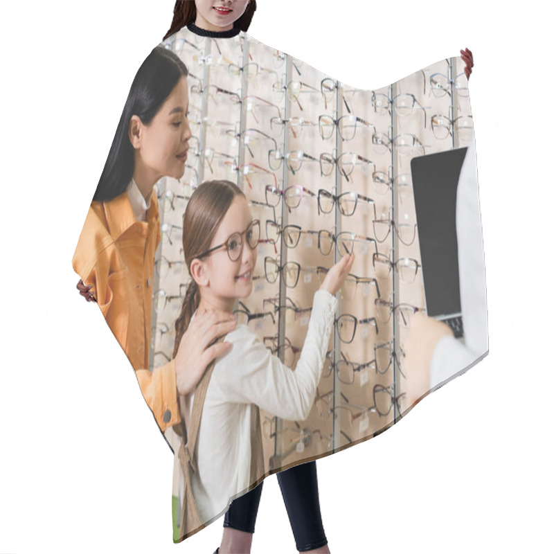 Personality  Smiling Girl Pointing At Assortment Of Eyeglasses Near Asian Mom And Blurred Oculist With Laptop In Optics Store Hair Cutting Cape