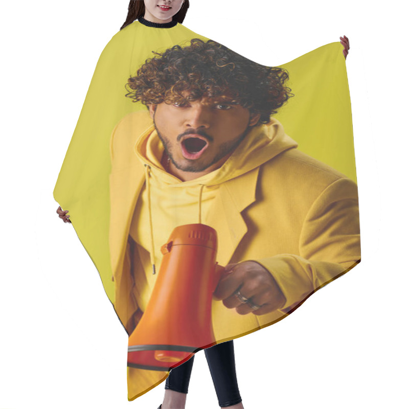 Personality  Young Man In Yellow Hoodie Holding Red And Orange Megaphone Against Vivid Backdrop. Hair Cutting Cape