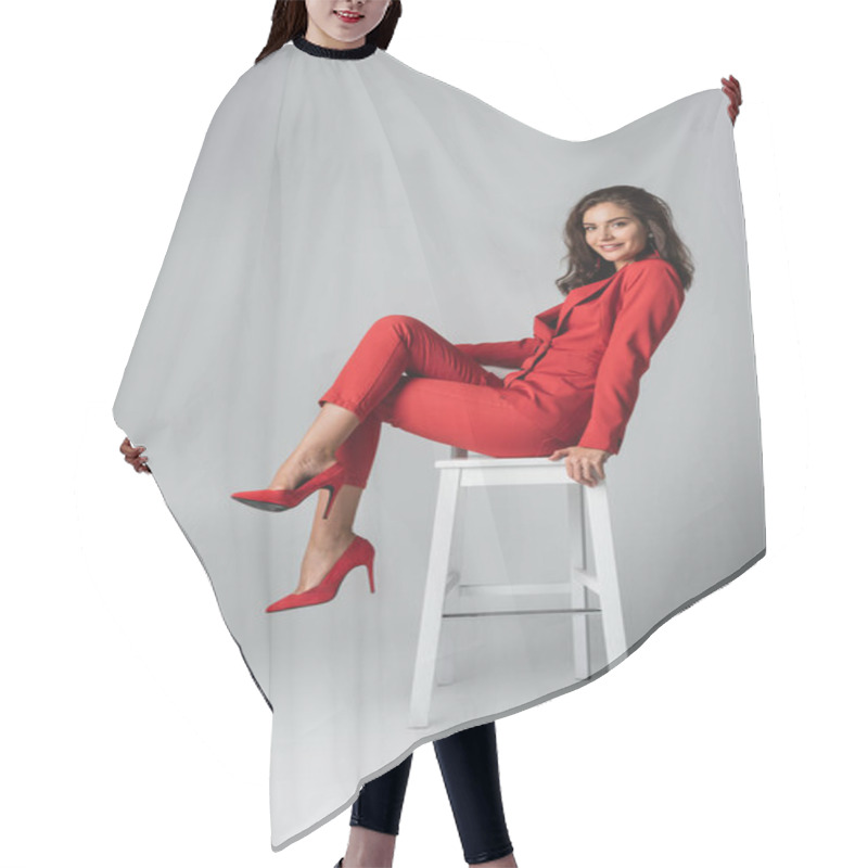 Personality  Full Length Of Positive Young Woman In Red Suit Posing While Sitting On White Chair On Grey Hair Cutting Cape