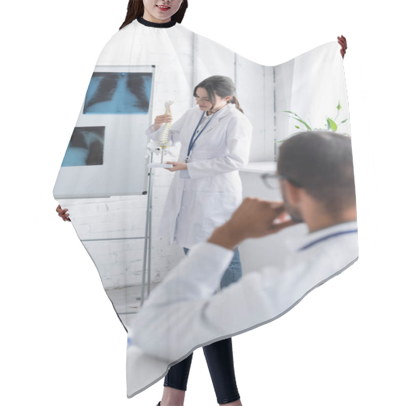 Personality  Young Doctor Holding Spine Model Neat Flip Chart With X-rays And Blurred Colleague  Hair Cutting Cape