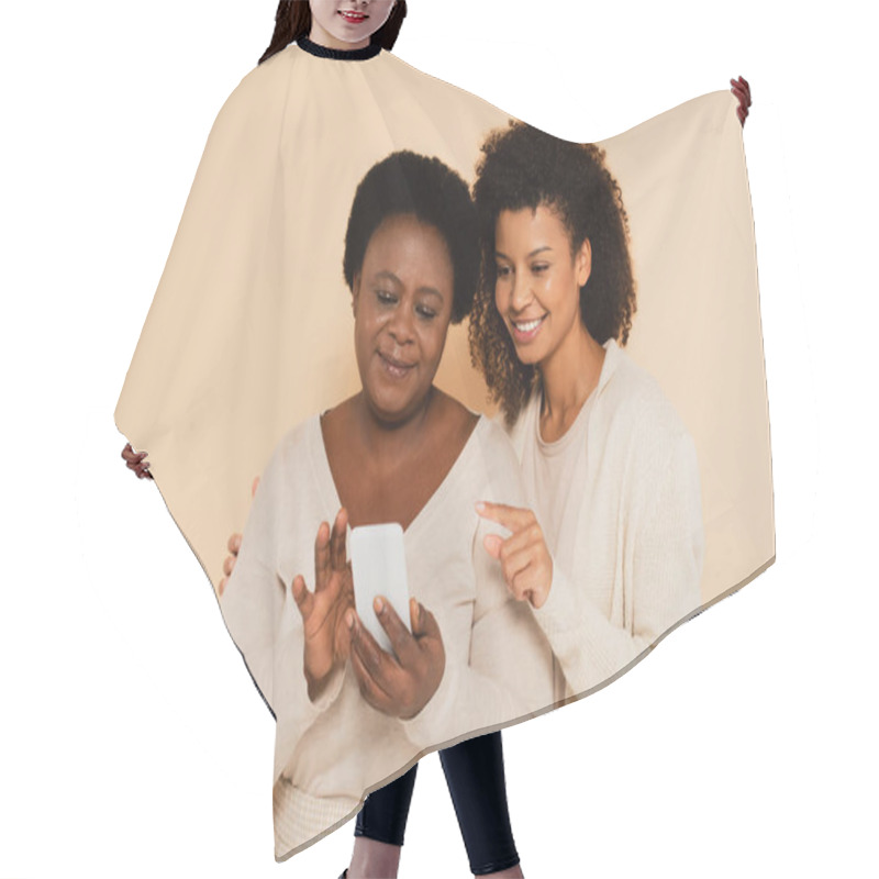 Personality  African American Adult Daughter Pointing With Finger To Smartphone In Hands Of Middle Aged Mother On Beige Background Hair Cutting Cape