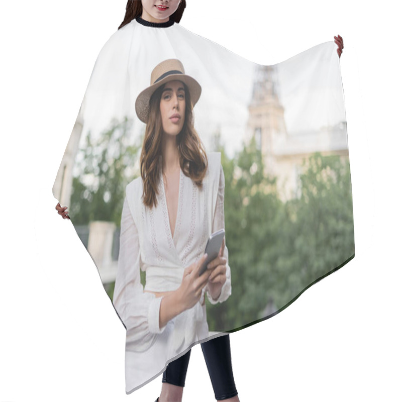 Personality  Stylish Woman In Sun Hat Holding Smartphone And Looking At Camera With Eiffel Tower At Background In Paris  Hair Cutting Cape