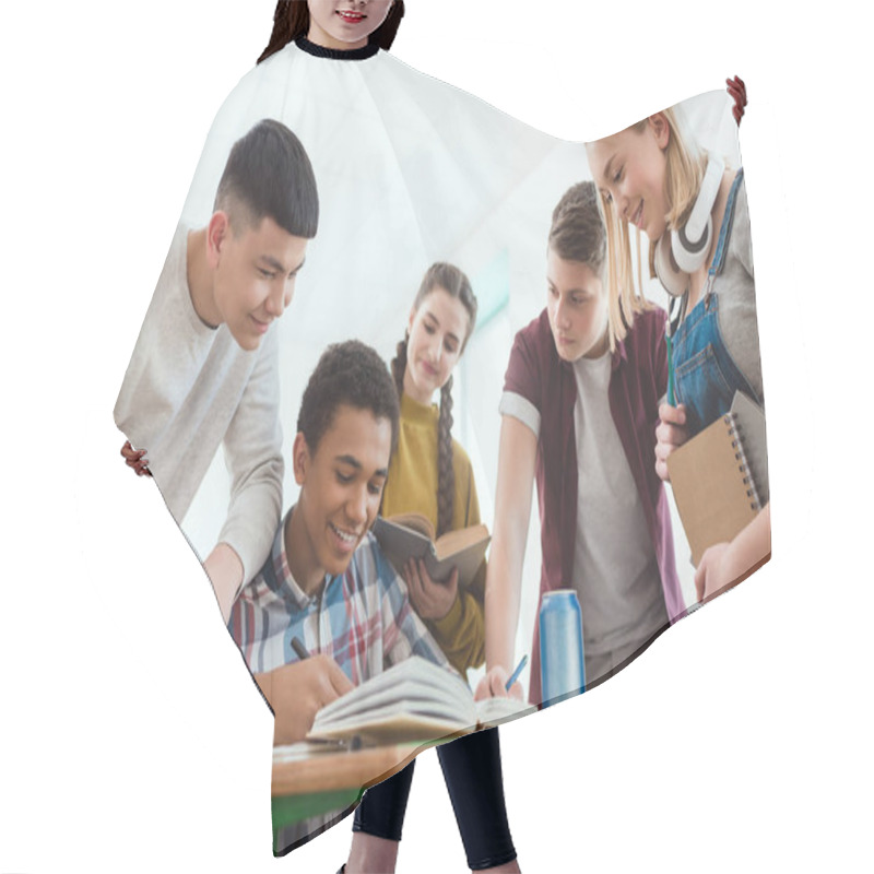 Personality  Smiling African American Schoolboy Writing In Notebook While His Classmates Standing Around Hair Cutting Cape