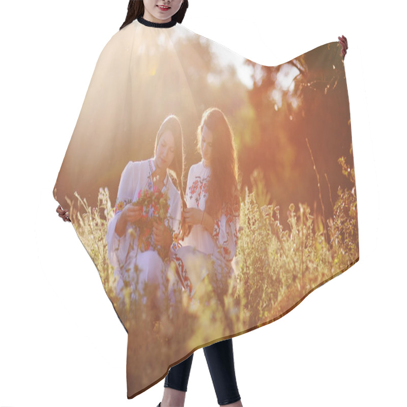 Personality  Two Young Pretty Girls In White Shirts Braid Each Other And Weave Wreaths Of Flowers Against The Background Of Grass And Nature At Sunset. Hair Cutting Cape