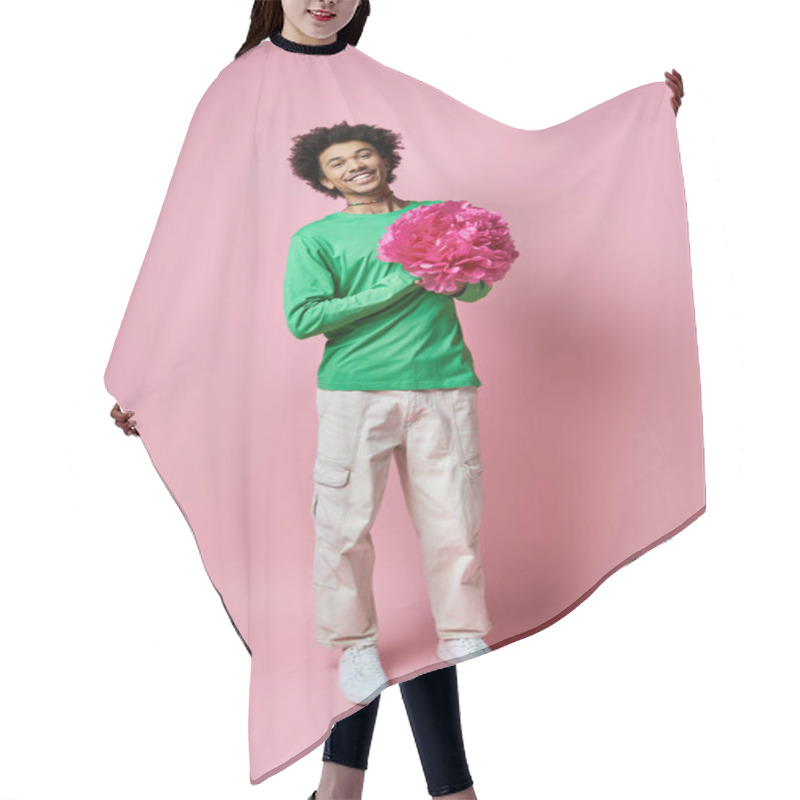 Personality  Cheerful Young African American Man In Green Shirt Holding A Delicate Pink Flower Against A Soft Pink Background. Hair Cutting Cape