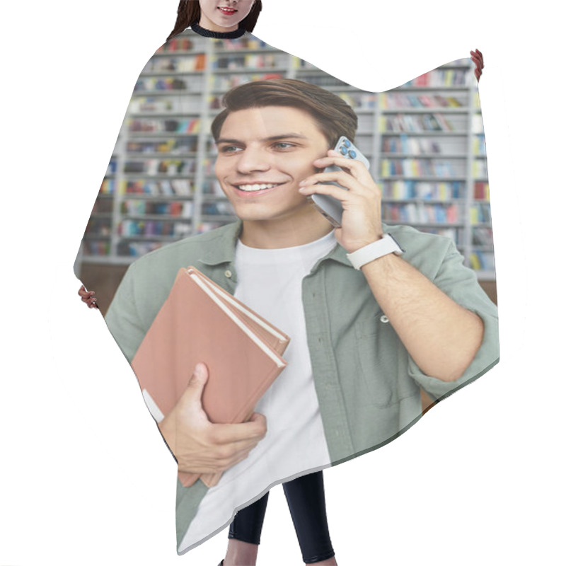 Personality  A Young Man Smiles And Holds Books While Chatting On His Phone In A Library. Hair Cutting Cape