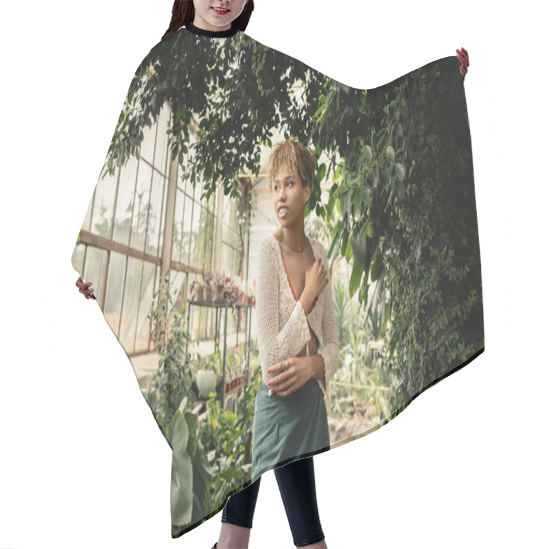 Personality  Smiling And Trendy Young African American Woman In Summer Knitted Top And Skirt Looking Away While Standing Near Green Plants In Garden Center, Stylish Woman Enjoying Lush Tropical Surroundings Hair Cutting Cape