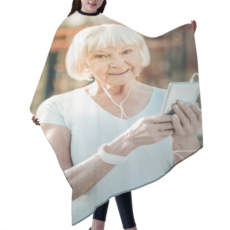 Personality  Keeping Phone In Hands. A Nice Old Lady Wearing Workout Clothing With A Sincere Smile And Short Grey Hair Keeping Her Phone In The Hands Being Outdoor. Hair Cutting Cape