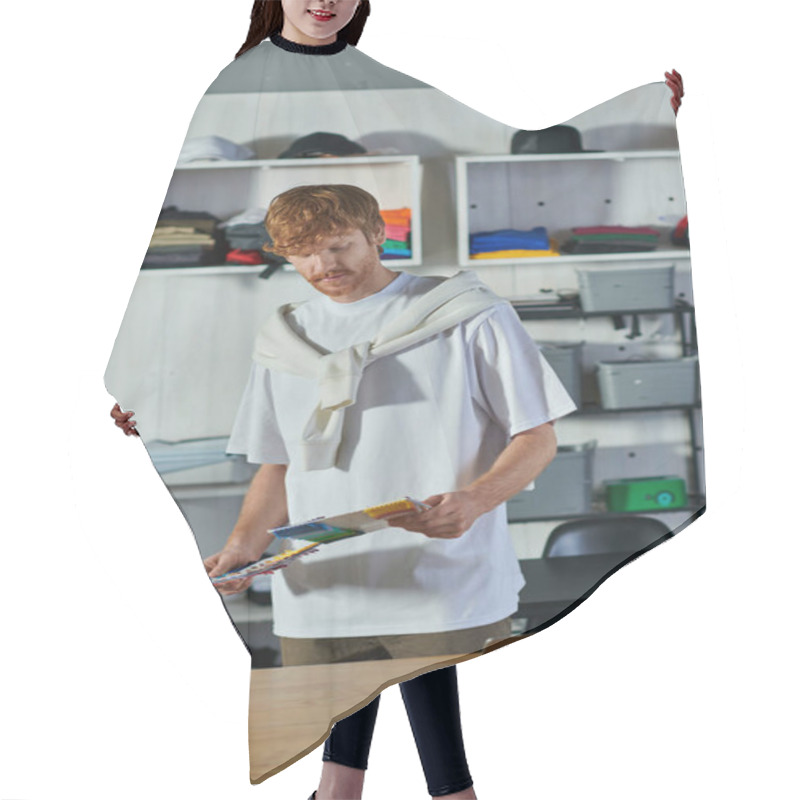 Personality  Young Redhead Craftsman In Casual Clothes Holding Cloth Samples While Working On Project Near Laptop On Table In Print Studio, Self-made Success Concept  Hair Cutting Cape