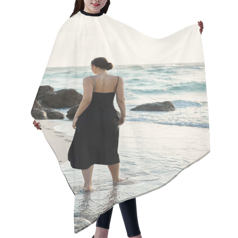 Personality  A Woman In A Black Sundress Walks Along A Sandy Beach, The Water Lapping At Her Feet. Hair Cutting Cape