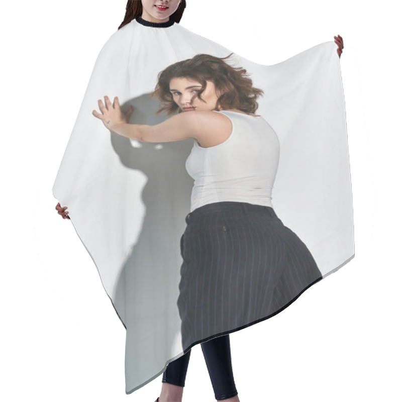 Personality  A Pretty Young Woman Striking A Pose In A White Tank Top And Black Pants In A Studio Against A Grey Background. Hair Cutting Cape