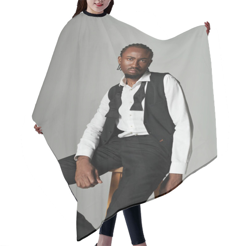 Personality  A Young Man Exudes Confidence In A Black Suit And Vest, Striking A Pose With Attitude On A Grey Background. Hair Cutting Cape