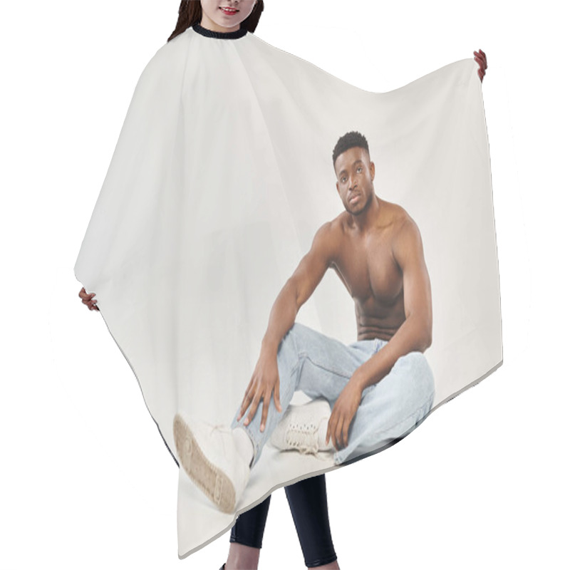 Personality  Young Shirtless African American Man Sitting On The Ground In A Studio With A Grey Background. Hair Cutting Cape