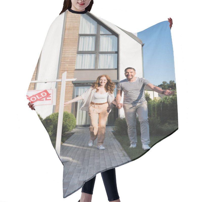 Personality  Cheerful Couple Holding Hands While Running Forward Near Sign With Sold Lettering And Modern House Hair Cutting Cape