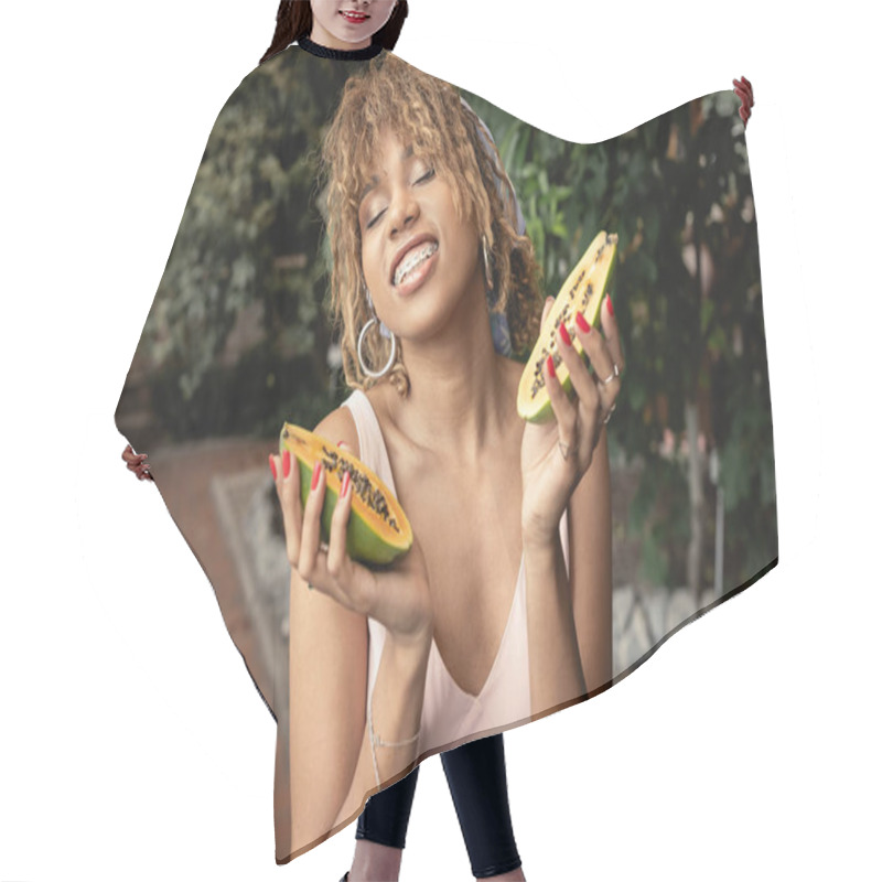 Personality  Smiling Young African American Woman With Braces Waring Summer Outfit And Closing Eyes While Holding Fresh Papaya In Blurred Indoor Garden, Fashion-forward Lady Inspired By Tropical Plants Hair Cutting Cape