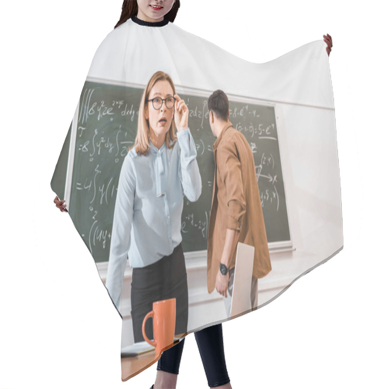 Personality  Female Teacher Standing Near Desk And Looking Surprised Near Student Hair Cutting Cape