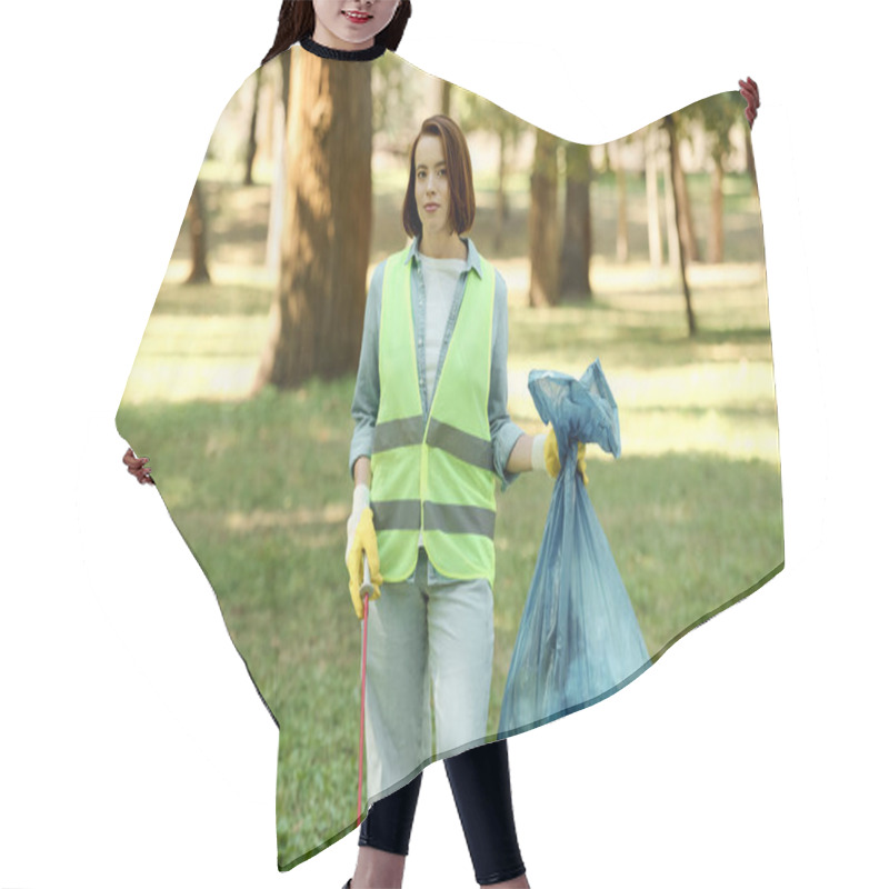 Personality  A Woman In A Green Safety Vest Holds A Blue Bag While Caring For Nature In A Park. Hair Cutting Cape