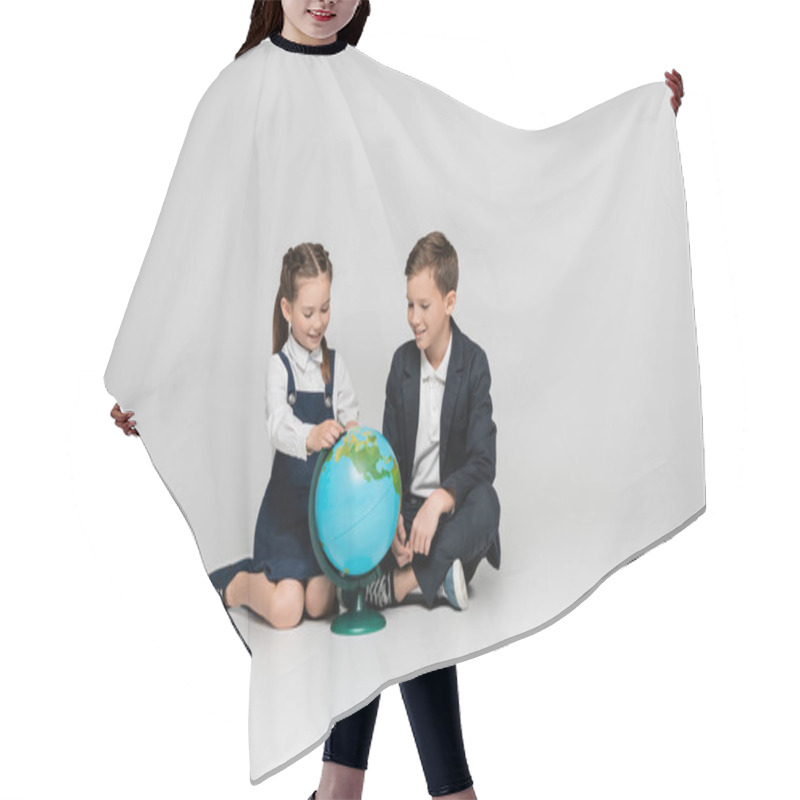 Personality  Happy Schoolgirl And Schoolboy Looking At Globe While Sitting On Grey Hair Cutting Cape