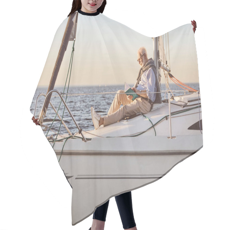 Personality  Relaxed Senior Man Reading A Book, While Sitting On The Side Of Sail Boat Or Yacht Deck Floating In Sea Hair Cutting Cape