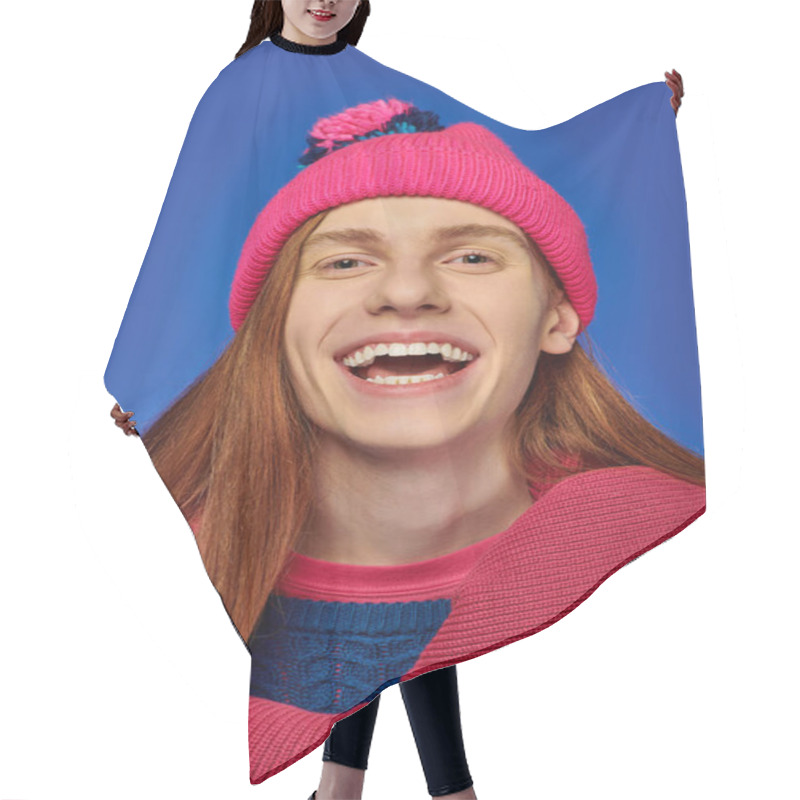 Personality  Emotional Young Man With Long Red Hair Laughs While Wearing A Vibrant Pink Hat And Sweater. Hair Cutting Cape