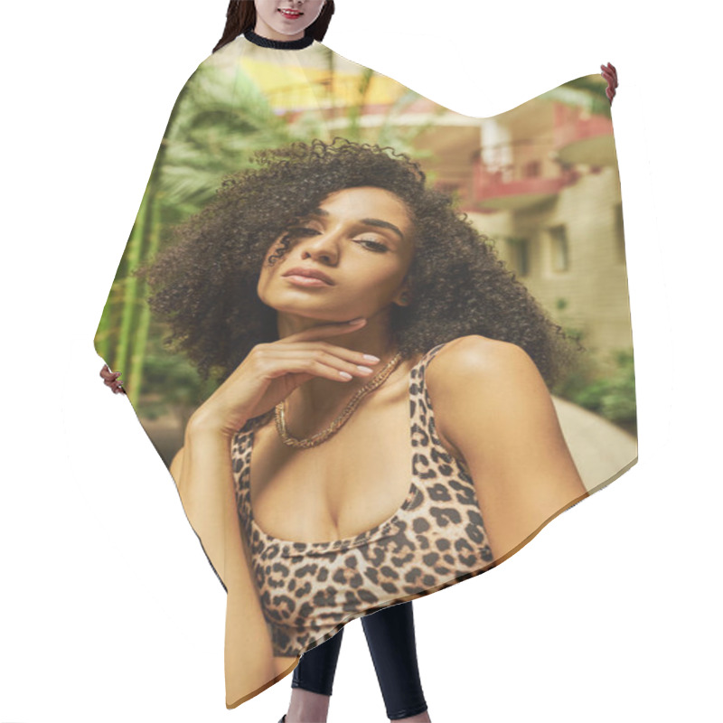 Personality  Curly Black Woman In Animal Print Attire Posing With Hand Near Face In Atrium With Green Plants Hair Cutting Cape