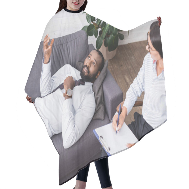 Personality  Selective Focus Of African American Man Gesturing And Talking While Lying On Sofa Near Psychologist With Pen And Clipboard Hair Cutting Cape